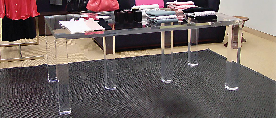 A glass display table showcasing neatly folded clothing items and black mugs in a retail store.